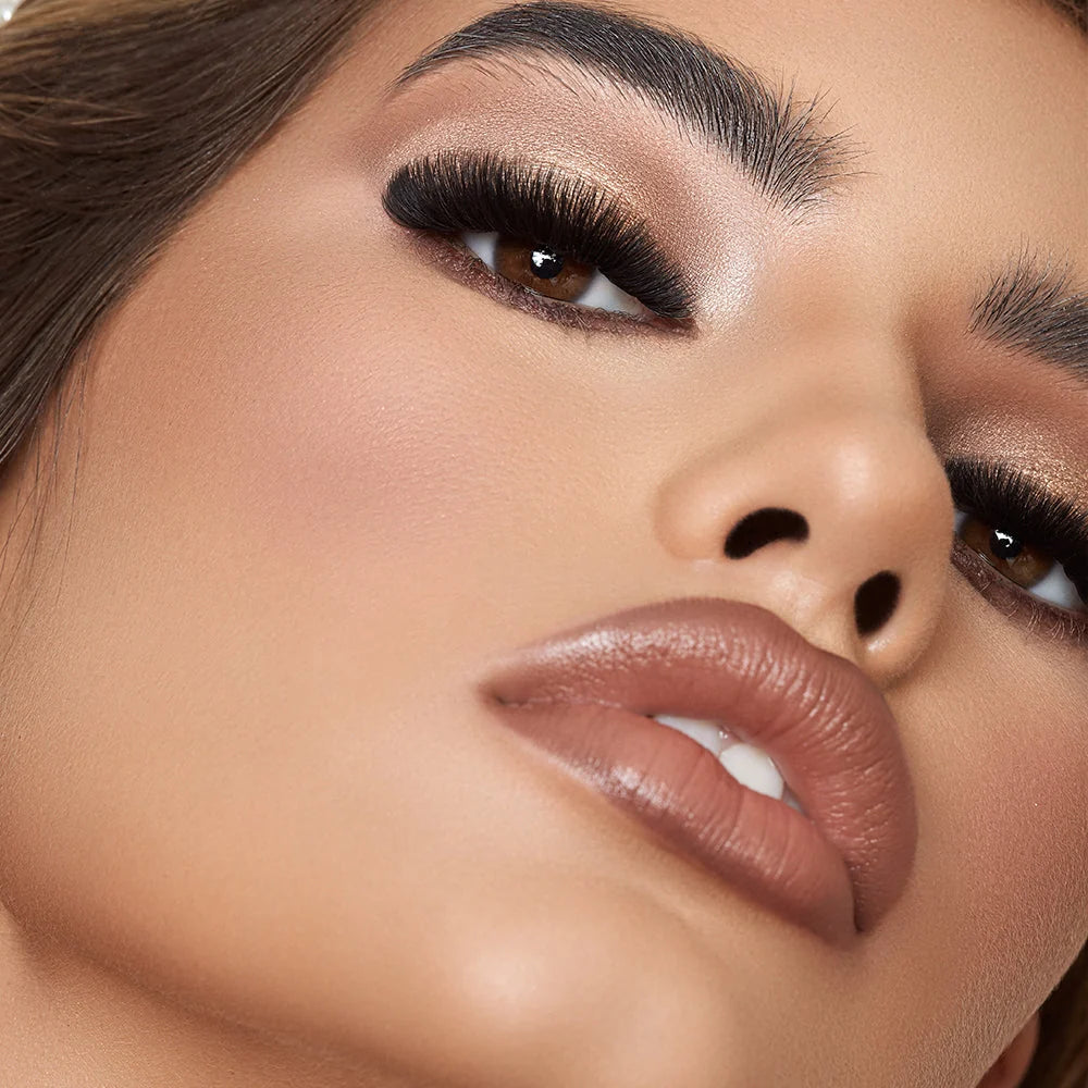 Close-up of a model's face showcasing a glossy, warm nude lip makeup look with defined eyebrows, hand made false eyelashes by lash box LA Australia, with sparkly warm-toned eyeshadow.