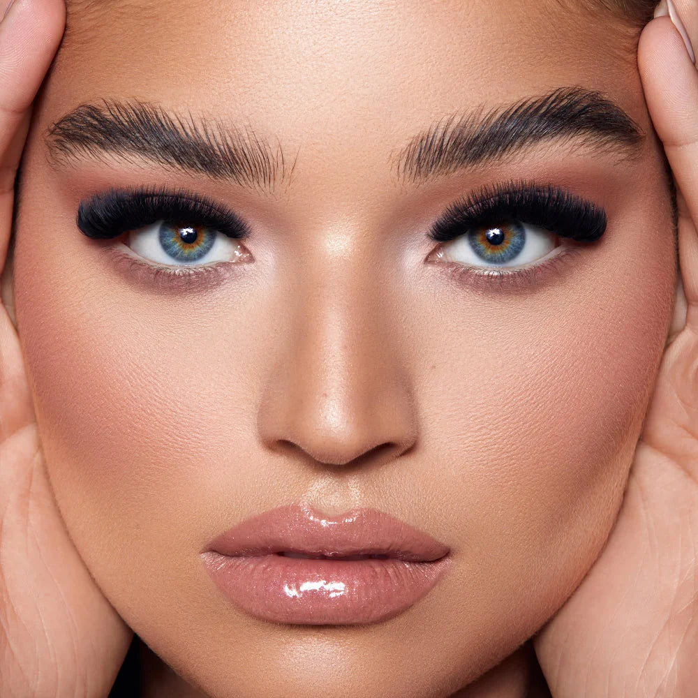 Close up pf a models face wearing LASH BOX LA hand crafted & well styled lash set, showcasing dramatic false eyelashes with long, curled black lashes and warm brown eyeshadow, paired with glossy nude-pink lips and well-defined eyebrows. Cashmere 0.03 favoite lashes and 0.05 0.07 