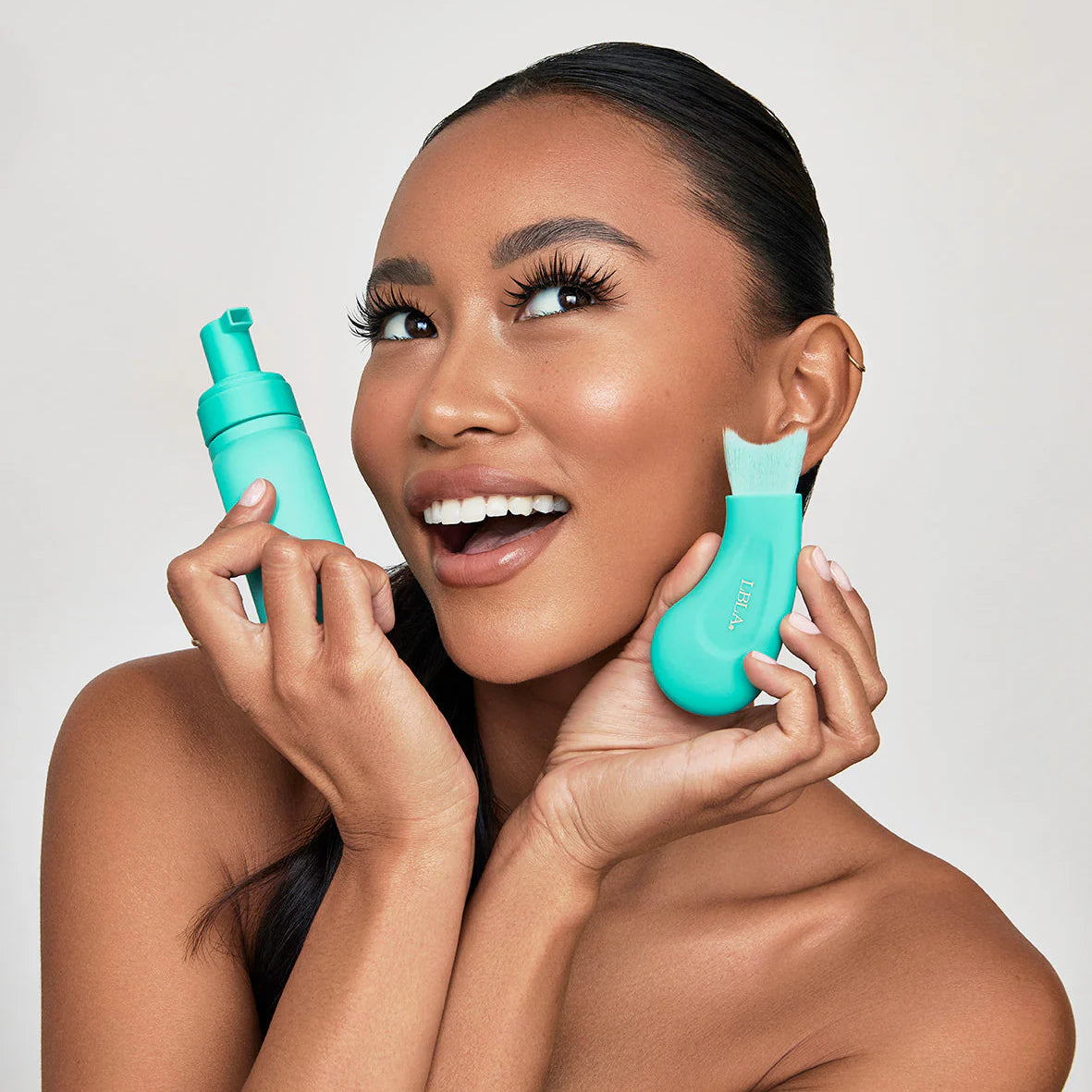 Woman holding two turquoise skincare bubble lash shampoo and eyelash cleansing brush against a plain background Woman applying a PH balanced Bubble lash shampoo product to her eyelashes with a teal ergonomic cleansing brush applicator. PH Balanced Lash Cleanser Botanical Bubble Lash Shampoo & cleansing brush. 
Size: 180ml
Key Ingredients:;Aloe Vera, Calendula, Chamomile, Rosemary, Lavender, Witch Hazel, Willow Bark, pH-balanced formula
Skin Type:All skin types including sensitive
