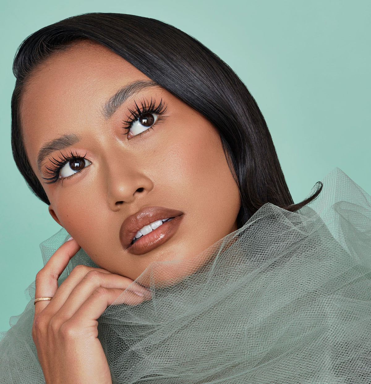 Woman with makeup and a light green background, showcasing lash box LA pixie lashes, special camellia style lashes blending multiple lengths and curls on one strip of lashes for easy to make soft texture sets of lashes. 